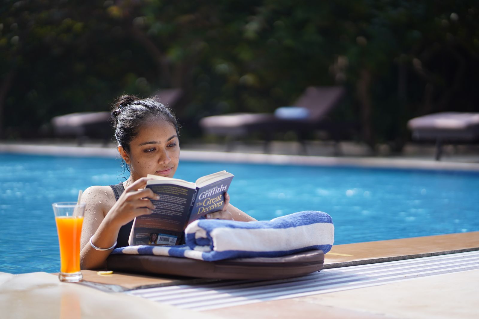 Guest reading by the pool with a drink